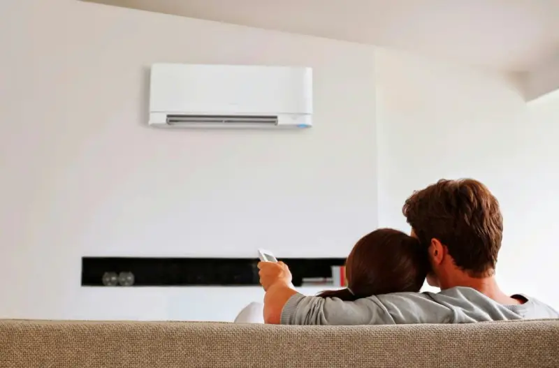 Pareja relajada en el sofá, disfrutando del confort que ofrece un **split aire acondicionado** en la pared.
