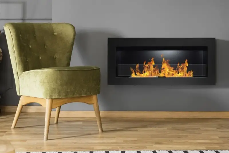 Sillón verde junto a chimenea moderna encendida. Un ejemplo de como encender la chimenea para crear un ambiente acogedor.